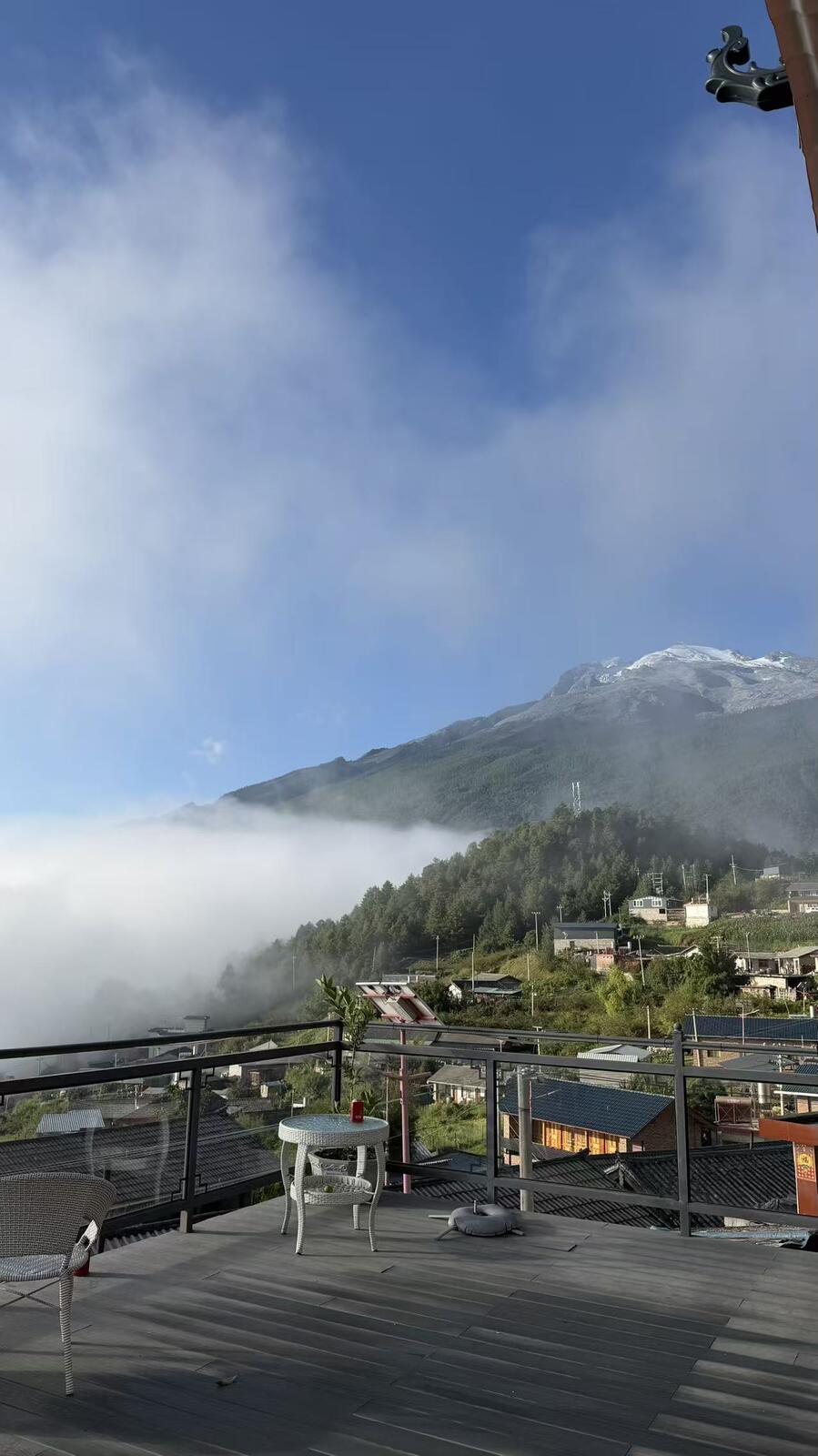 Guesthouse rooftop terrace in Haba Yi Village, with a cloud inversion filling the valley and Haba's snow-capped upper slopes behind.