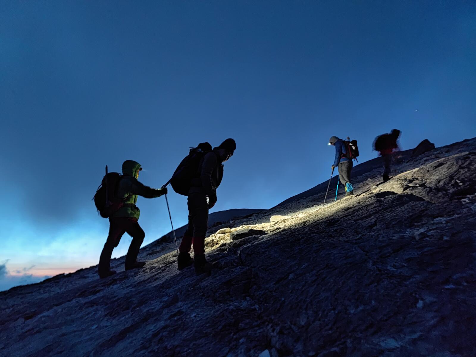 Climbers silhouetted against the sky as dawn breaks over the ridge.