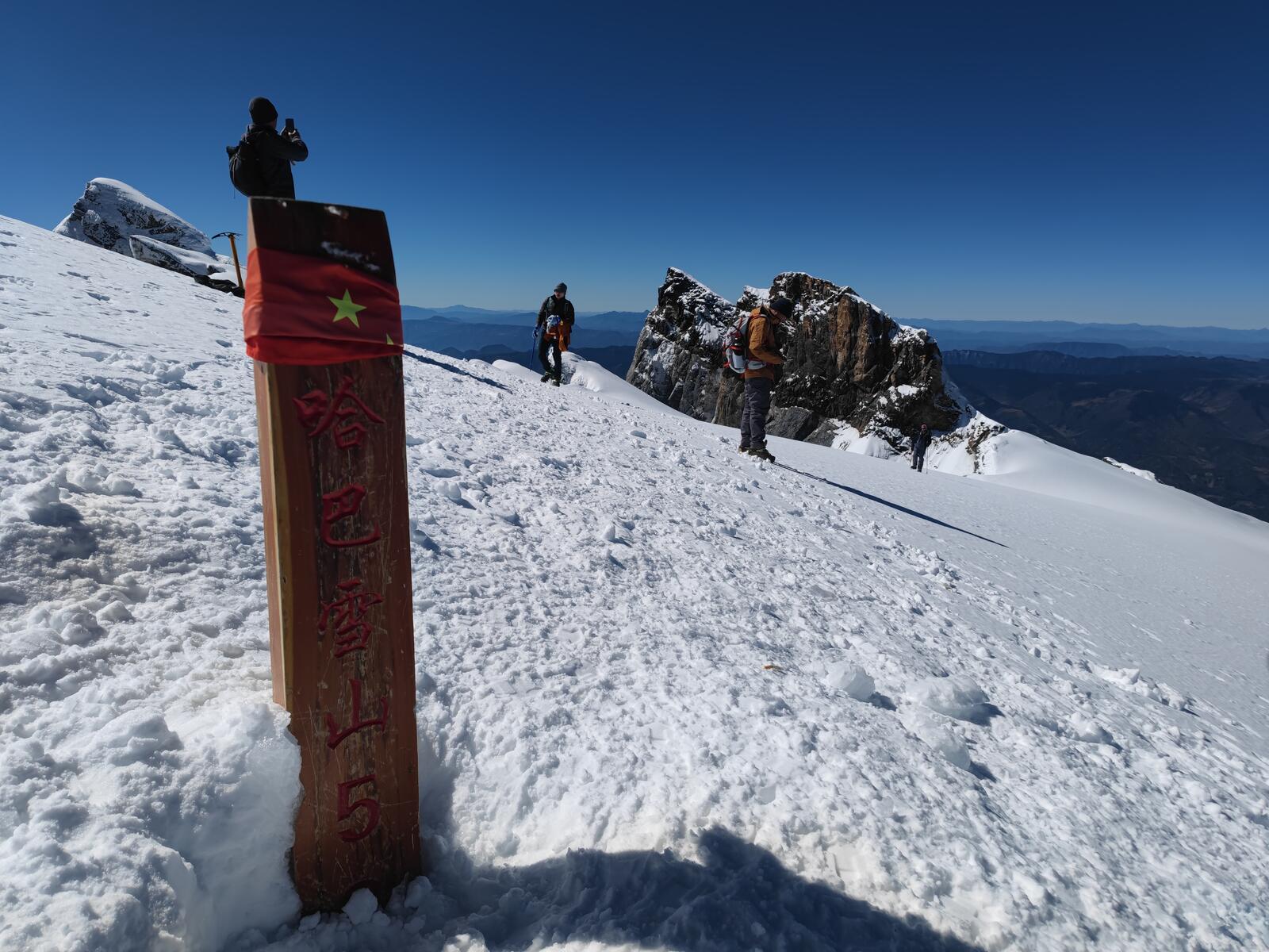 Climbers at the summit sign under a clear, deep blue sky.